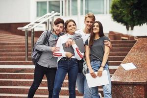 abrazándose unos a otros. grupo de jóvenes estudiantes con ropa informal cerca de la universidad durante el día foto