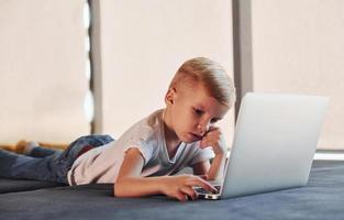Little boy in casual clothes lying down on the ground with laptop photo