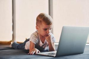 Little boy in casual clothes lying down on the ground with laptop photo