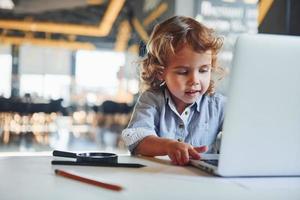 Smart child in casual clothes using laptop for education purposes or fun photo