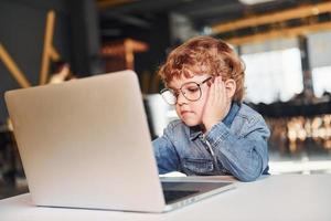 Smart child in casual clothes and in glasses using laptop for education purposes photo