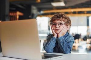 niño inteligente con ropa informal y gafas usando una laptop con fines educativos foto