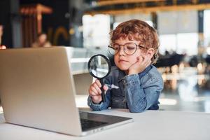 Smart child in casual clothes and in glasses using laptop for education purposes photo