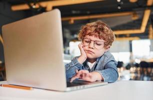 niño inteligente con ropa informal y gafas usando una laptop con fines educativos foto