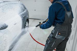 Male worker in uniform washing new modern car that covered with soap. Conception of service photo