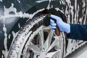 Male worker in uniform washing new modern car that covered with soap. Conception of service photo