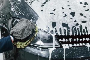 Male worker in uniform washing new modern car that is full of soap. Conception of service photo