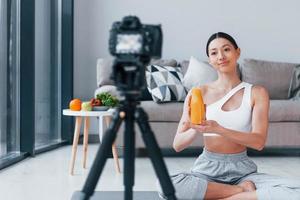 Blogger young woman with slim body shape in sportswear talking about vegetables, fruits and healthy food indoors at home photo