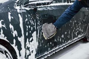 Male worker in uniform washing new modern car that is full of soap. Conception of service photo