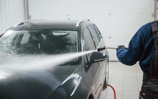 Male worker in uniform washing new modern car indoors. Conception of service photo