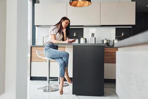 Young beautiful brunette in casual clothes sits in kitchen with fresh drink at morning time photo