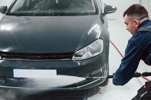 Male worker in uniform washing new modern car indoors. Conception of service photo