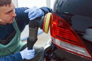 trabajador masculino en uniforme puliendo un coche nuevo y moderno. concepto de servicio foto