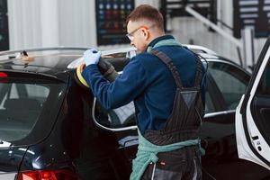 Male worker in uniform polishing new modern car. Conception of service photo