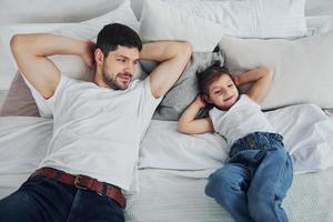 Happy father with his daughter spending free time at home together. Lying down on bed photo