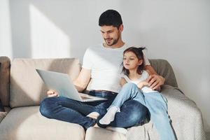 Happy father with his daughter spending free time with laptop at home together photo