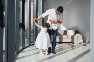 Happy father with his daughter in dress learning how to dance at home together photo