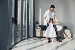 Happy father with his daughter in dress learning how to dance at home together photo