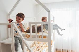 dos niños pequeños descansan y se divierten juntos en el interior del dormitorio. gato acostado foto