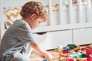 Cute little boy sitting and have fun indoors in the bedroom with plastic construction set photo