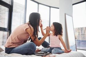 aprendiendo a maquillarme. joven madre con su hija pasando el fin de semana juntos en la habitación foto