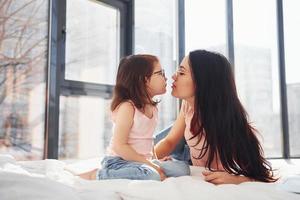 Young mother with her daughter spending weekend together in room and giving a kiss photo