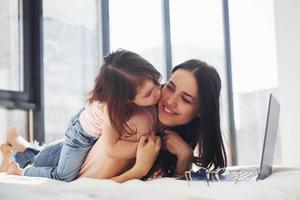 joven madre con su hija pasando el fin de semana juntos en la habitación y usando una laptop foto