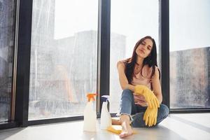 la mujer se sienta en el alféizar de la ventana con botellas de spray de limpieza y con guantes foto