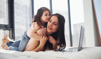 Young mother with her daughter spending weekend together in room and using laptop photo