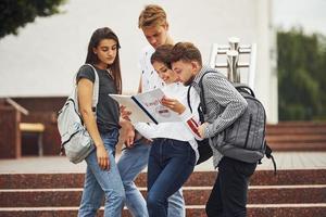 leyendo el libro. grupo de jóvenes estudiantes con ropa informal cerca de la universidad durante el día foto