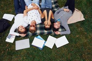 Having good rest. Group of young students in casual clothes on green grass at daytime photo