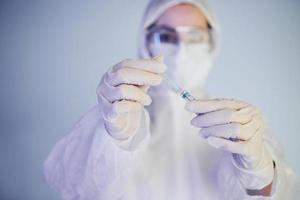 Holds syringe. Portrait of female doctor scientist in lab coat, defensive eyewear and mask photo