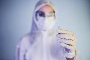 Holds syringe. Portrait of female doctor scientist in lab coat, defensive eyewear and mask photo