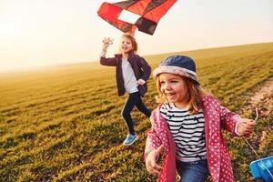 Two little girls friends have fun together with kite and toy car on the field at sunny daytime photo