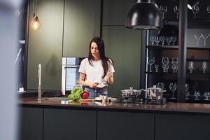 verduras y leche en la mesa. preparando comida. joven hermosa morena con ropa informal en el interior de la cocina durante el día foto