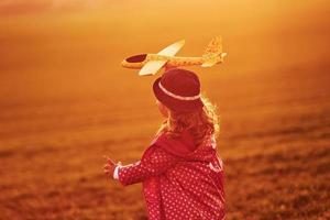 Illuminated by sunlight. Cute little girl have fun with toy plane on the beautiful field at daytime photo