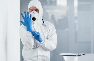 Male doctor scientist in lab coat, defensive eyewear and mask wearing blue gloves photo