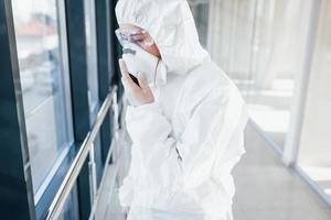 Female doctor scientist in lab coat, defensive eyewear and mask standing indoors photo
