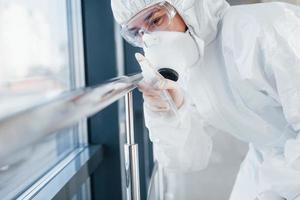 Female doctor scientist in lab coat, defensive eyewear and mask standing indoors with antibacterial spray photo