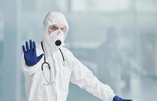 Shows stop gesture by hand. Male doctor scientist in lab coat, defensive eyewear and mask photo