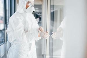 Female doctor scientist in lab coat, defensive eyewear and mask standing indoors and wearing gloves photo