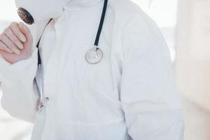 Feels bad and sick. Female doctor scientist in lab coat, defensive eyewear and mask standing indoors photo