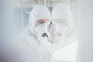 Feels bad and sick. Female doctor scientist in lab coat, defensive eyewear and mask standing indoors photo