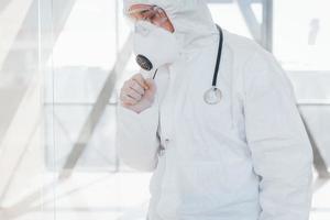 Feels bad and sick. Female doctor scientist in lab coat, defensive eyewear and mask standing indoors photo