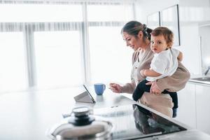 Female blogger mother with her kid together indoors at home at weekend using tablet photo