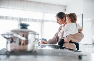 Female blogger mother with her kid together indoors at home at weekend using tablet photo