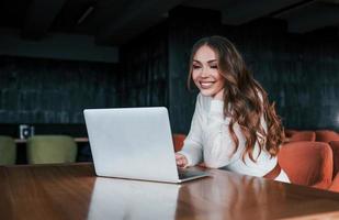 Successful young woman in white dress sits by table with laptop photo