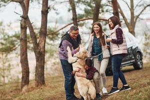 Happy family have fun with their active dog near modern car outdoors in forest photo