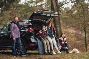 la familia feliz se divierte con su perro cerca de un camión moderno al aire libre en el bosque foto