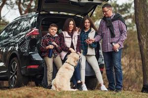 la familia feliz se divierte con su perro cerca de un camión moderno al aire libre en el bosque foto